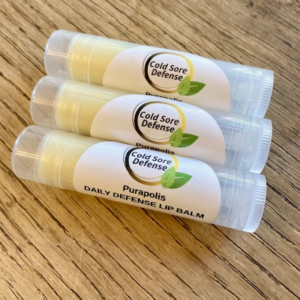 3-pack of Purapolis Cold Sore Defense Daily Defense lip balms on a wooden tabletop, made with a healing blend of olive oil, lemon balm, organic coconut oil, shea butter, propolis, and sunflower oil for natural cold sore protection and daily lip nourishment.