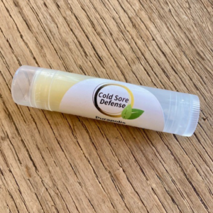 Purapolis Cold Sore Defense Daily Defense lip balm on a wooden tabletop, made with olive oil, lemon balm, organic coconut oil, shea butter, propolis, and sunflower oil for natural cold sore protection and daily lip care.